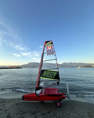 A red WASZP, sail number CAN 2091, rigged on its dolly at the water’s edge.